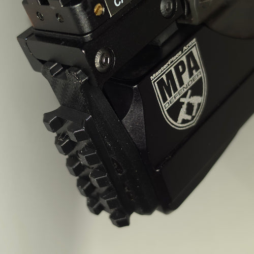 Close-up of a black tactical firearm accessory with a textured grip and a visible MPA Defender logo on a light gray background.